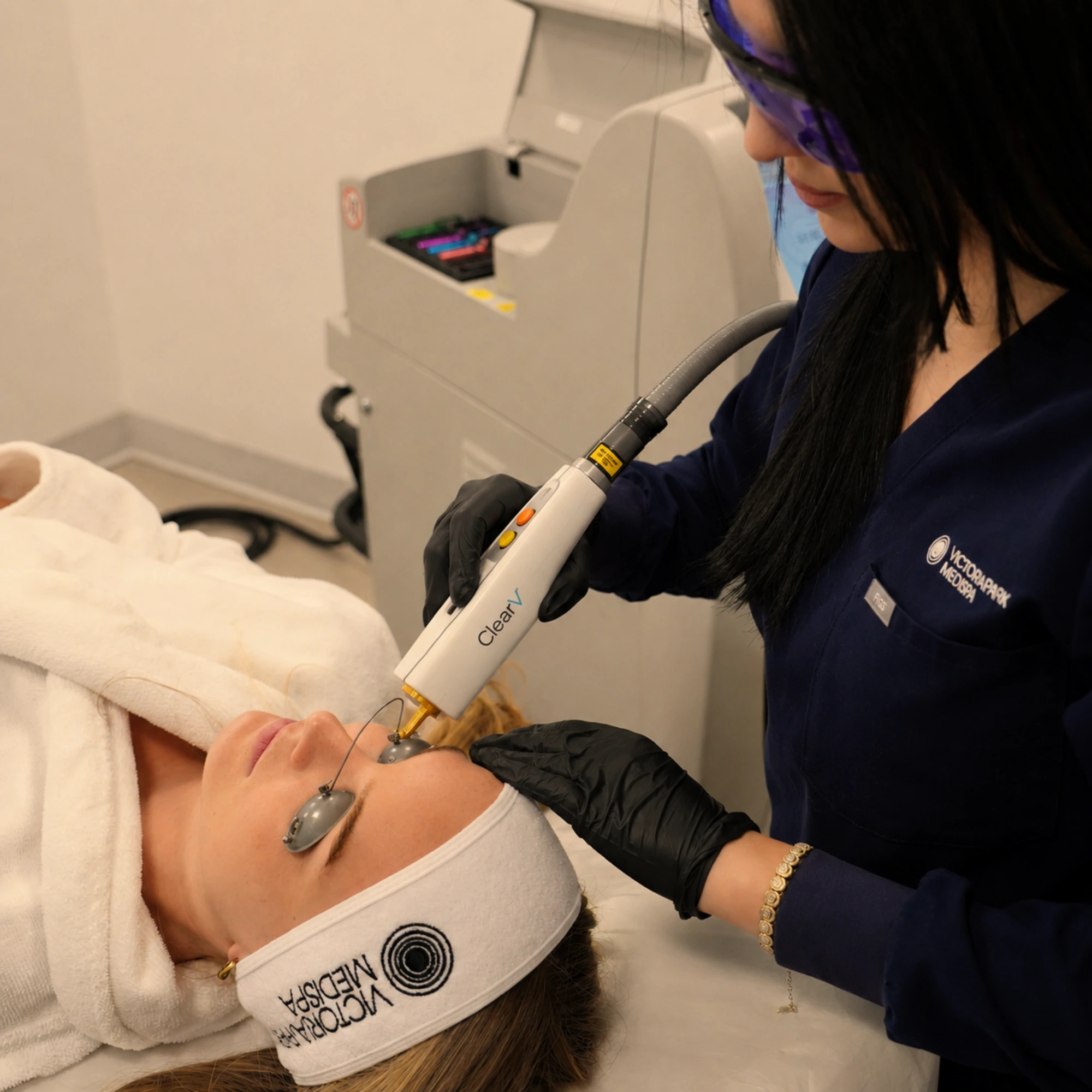 Medical professional performing a ClearV laser treatment on the face using the ClearV handpiece while the patient wears protective metal eye shields.